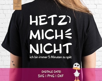 Puede incluir: Una camiseta negra con texto blanco que dice HETZ MICH NICHT y ich bin immer 5 Minuten zu spät. El diseño incluye una pequeña flecha y líneas gráficas. Una etiqueta marrón con el texto PLOTTEN MIT SANDRA está unida a la camiseta.