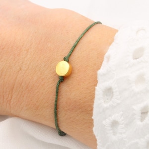 Op de afbeelding: Een groene armband van touw met een ronde gouden bedel.