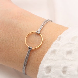Könnte beinhalten: Ein graues Kordelarmband mit einem goldenen Kreisanhänger.