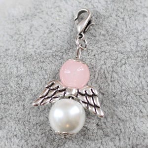 hell Rosa mit weißer Schutzengel Anhänger auf einem grauen Kissen liegend