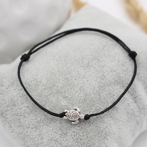 Op de afbeelding: Een zwart koord armband met een zilveren schildpad bedel.