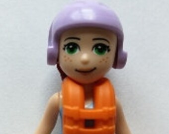 Puede incluir: Una figura de Lego con un casco morado, un chaleco salvavidas, pantalones cortos verdes y sandalias moradas.