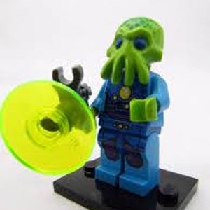May include: A Lego minifigure of an alien with a green head and tentacles, wearing a blue suit. The figure is holding a black tool and a yellow disc. The minifigure is standing on a black base.