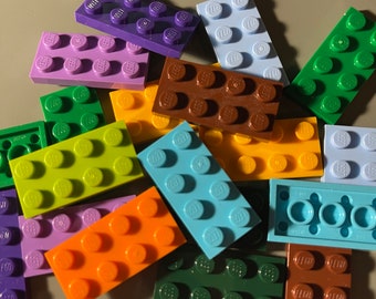 Puede incluir: Una colección de ladrillos LEGO de colores en varios tonos de verde, azul, morado, naranja, marrón y amarillo. Los ladrillos son todos de tamaño 1x2 y tienen el logotipo de LEGO impreso en ellos.