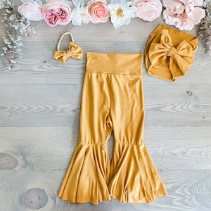 May include: A mustard yellow baby outfit with a matching headband and a bow. The outfit includes a pair of flared pants and a headband with a bow.