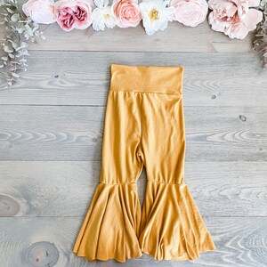 May include: Mustard yellow flared pants with a wide waistband. The pants have a wide leg and a flowy, bell-bottom style.