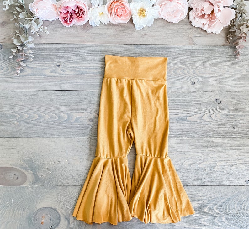 May include: Mustard yellow flared pants with a wide waistband. The pants have a wide leg and a flowy, bell-bottom style.