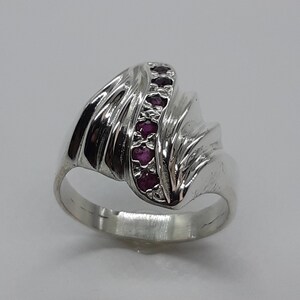 May include: A silver ring with a wave-like design and a row of pink gemstones.