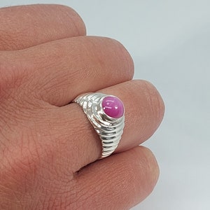 Op de afbeelding: Een zilveren ring met een roze edelsteen in een getextureerde band.