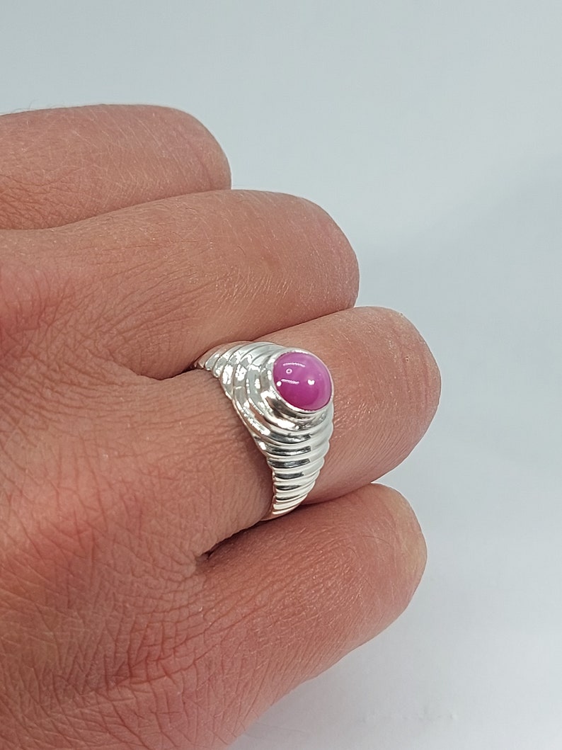 Op de afbeelding: Een zilveren ring met een roze edelsteen in een getextureerde band.