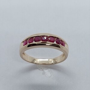 May include: A gold band ring with a row of red ruby stones set in the centre.