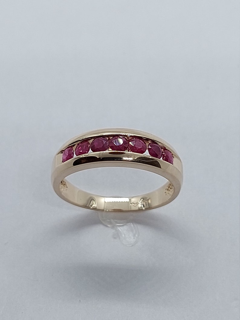 May include: A gold band ring with a row of red ruby stones set in the centre.