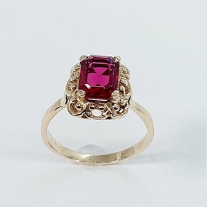May include: A gold ring with a red gemstone set in a filigree design.