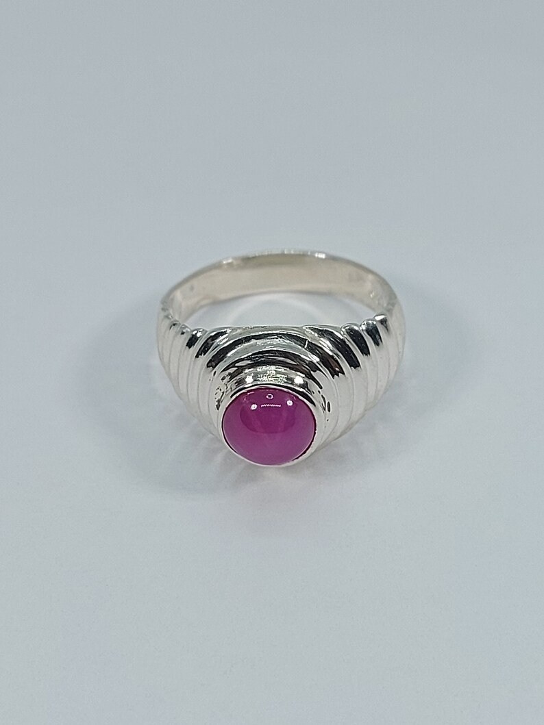 K&ouml;nnte beinhalten: Ein silberner Ring mit einem rosafarbenen Edelstein, der in eine strukturierte Band gefasst ist.