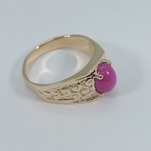 Op de afbeelding: Een gouden ring met een roze edelsteen gezet in een getextureerde band.