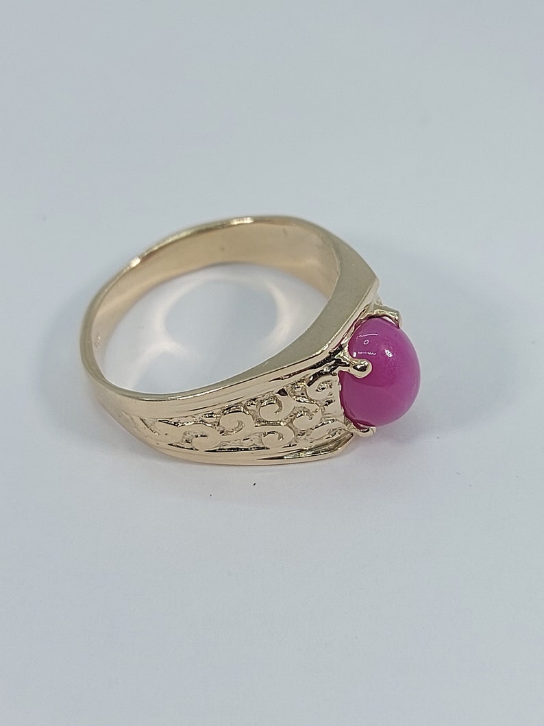 Op de afbeelding: Een gouden ring met een roze edelsteen gezet in een getextureerde band.
