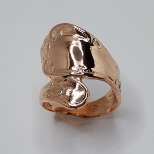 May include: A rose gold ring with a unique design. The ring is made of a single piece of metal that is bent and shaped to create a unique design. The ring is smooth and polished.
