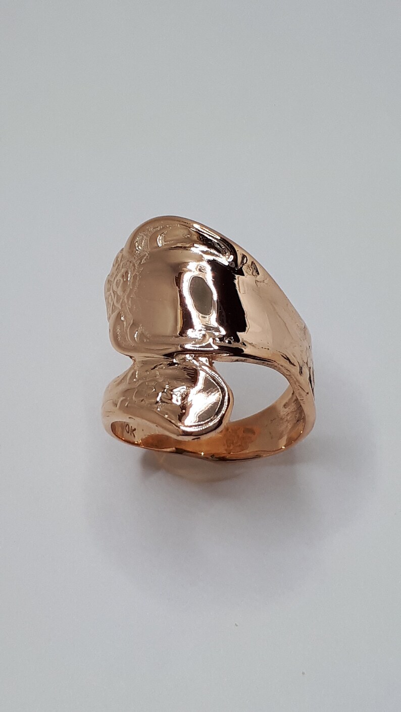 May include: A rose gold ring with a unique design. The ring is made of a single piece of metal that is bent and shaped to create a unique design. The ring is smooth and polished.