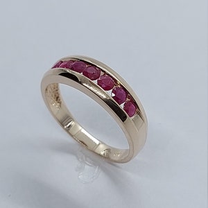 May include: A gold band ring with a row of red ruby stones set in the band.