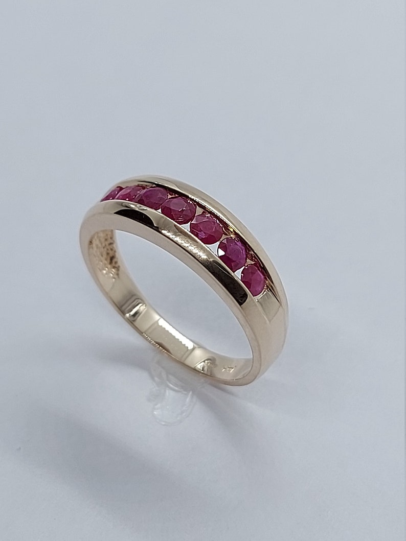 May include: A gold band ring with a row of red ruby stones set in the band.
