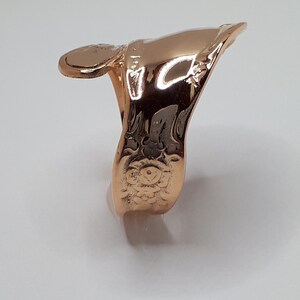 May include: A gold-toned finger ring with a decorative design. The ring is made of metal and has a smooth, polished finish.
