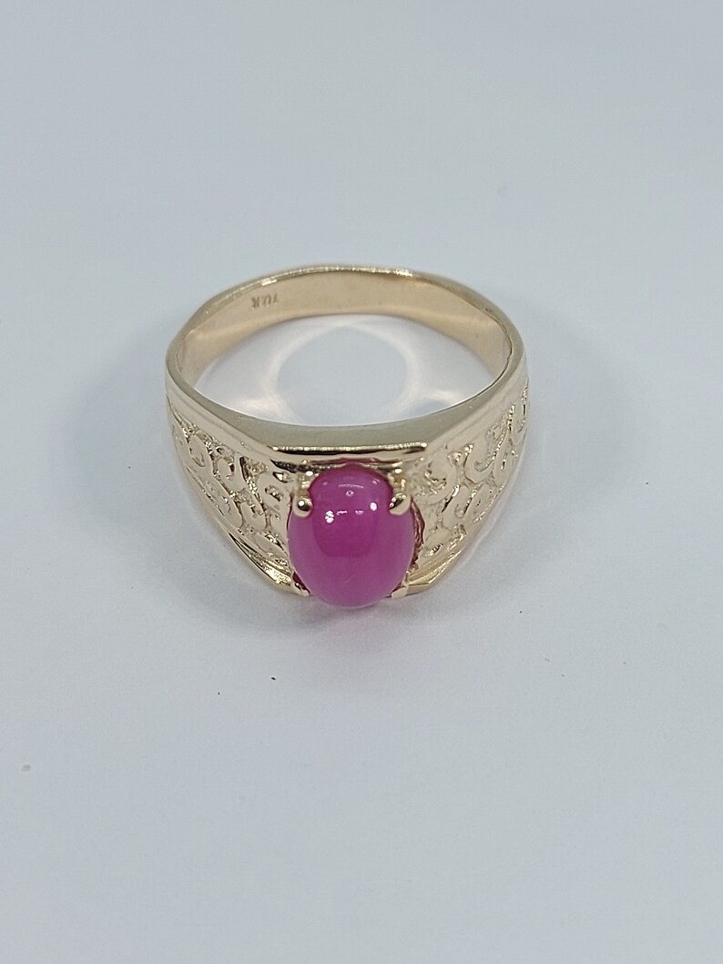 Op de afbeelding: Een gouden ring met een ovale roze edelsteen in het midden. De ring heeft een gedetailleerd ontwerp rond de edelsteen.