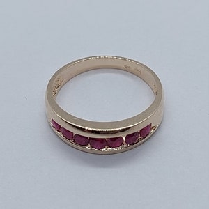 May include: A gold band ring with a row of red ruby stones set in the band.