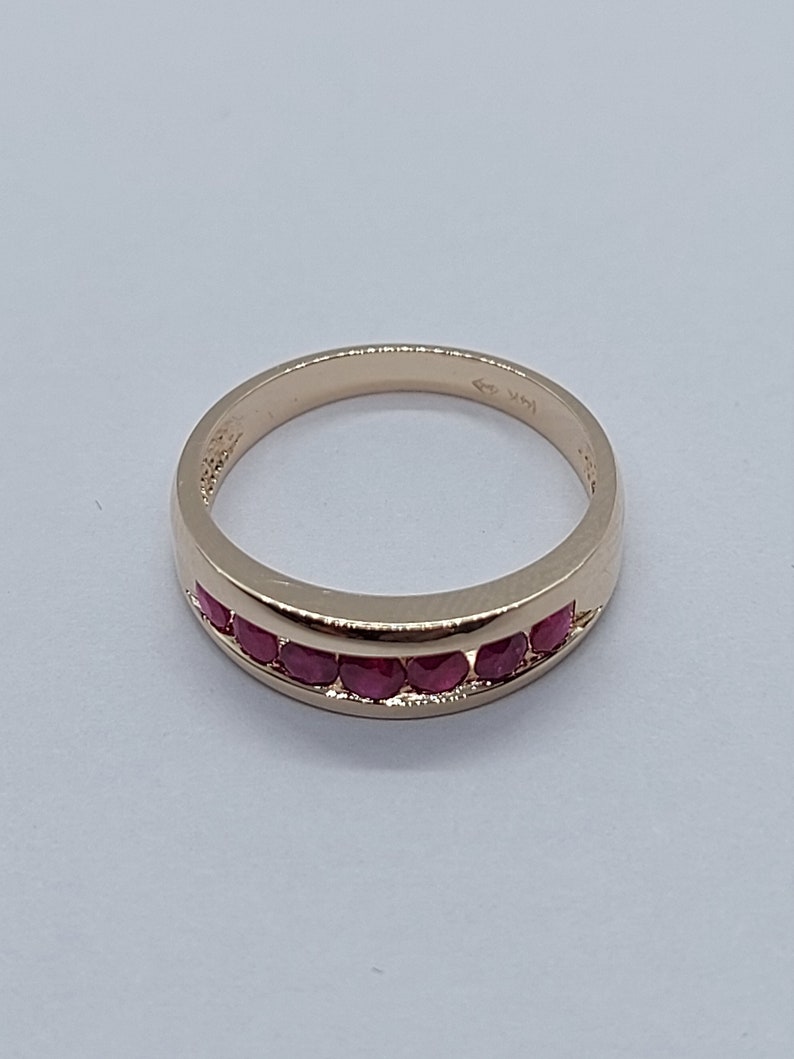 May include: A gold band ring with a row of red ruby stones set in the band.