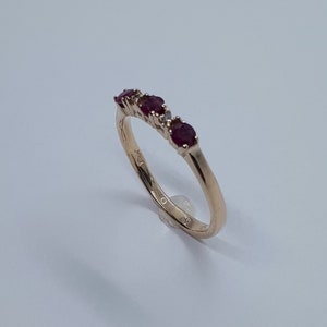 May include: A gold band ring with five red gemstones and a single diamond. The ring is set on a white background.