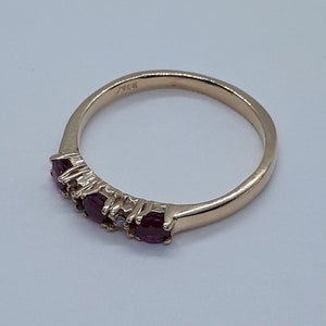 May include: A gold band ring with five red gemstones and one clear gemstone. The ring is marked "14K" on the inside.
