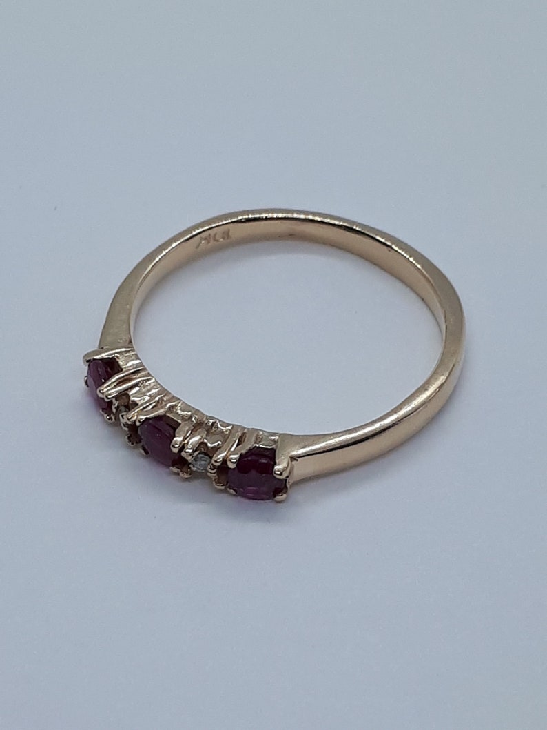 May include: A gold band ring with five red gemstones and one clear gemstone. The ring is marked "14K" on the inside.
