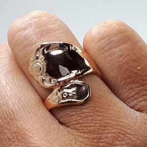May include: A gold-toned ring with a unique, abstract design. The ring is made of two pieces that are joined together, creating a twisted, asymmetrical look.