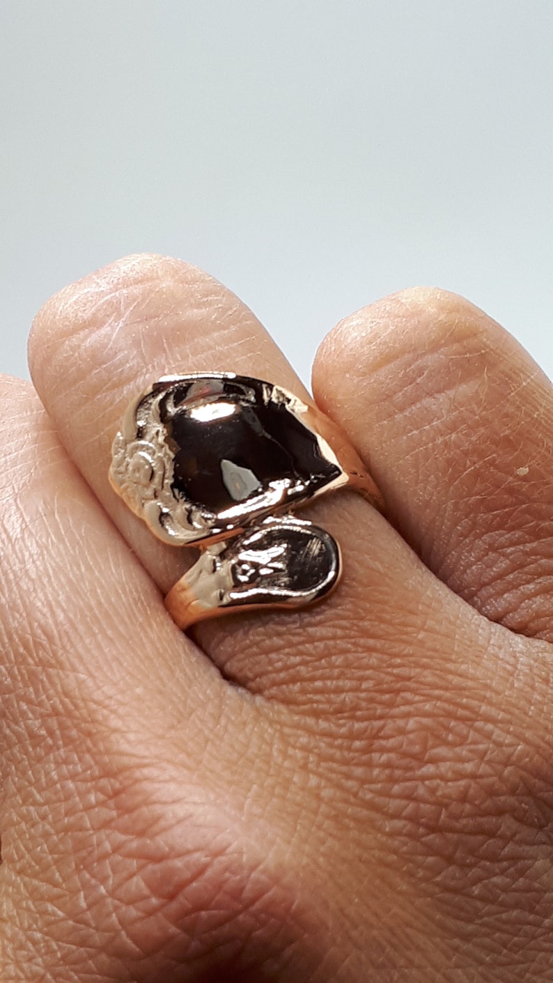 May include: A gold-toned ring with a unique, abstract design. The ring is made of two pieces that are joined together, creating a twisted, asymmetrical look.