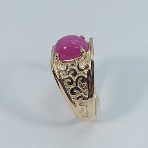 Op de afbeelding: Een gouden ring met een roze ovale edelsteen gezet in een filigraan ontwerp.
