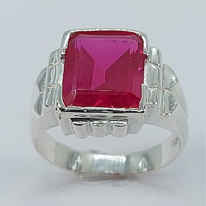 May include: A silver ring featuring a large, square, pink gemstone set in an ornate design.