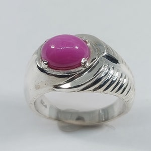 Op de afbeelding: Een zilveren ring met een grote, ovale, magenta edelsteen. De ring heeft een textuurontwerp aan de zijkanten en een gepolijste afwerking. De edelsteen is gezet in een bezel setting. Een opvallend sieraad.