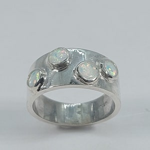 May include: A silver band ring with four white opal stones set into the band.