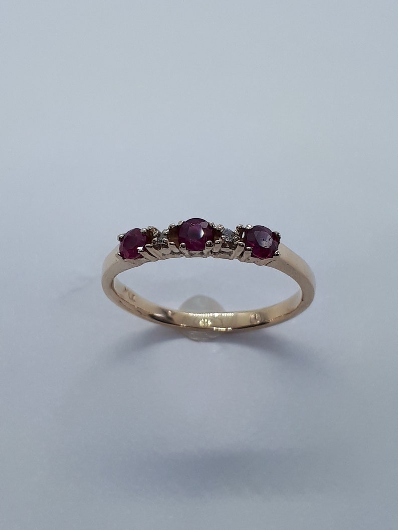 May include: A gold band ring with five red gemstones and two small diamonds. The ring is set on a white background.
