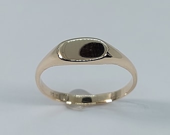 May include: A gold signet ring with a smooth, oval-shaped top. The ring is simple and elegant.