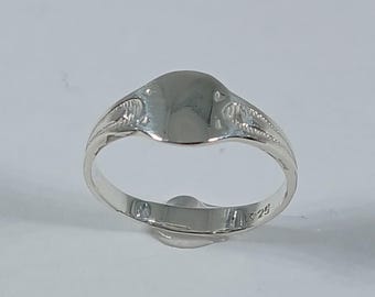 May include: A polished silver signet ring with an oval face and decorative detailing on the shoulders. The ring is set against a white background, showcasing its reflective surface. The ring is a classic piece of jewelry.
