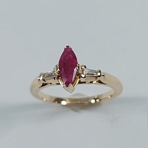 May include: A gold ring featuring a marquise-shaped ruby gemstone with two smaller diamond accents.