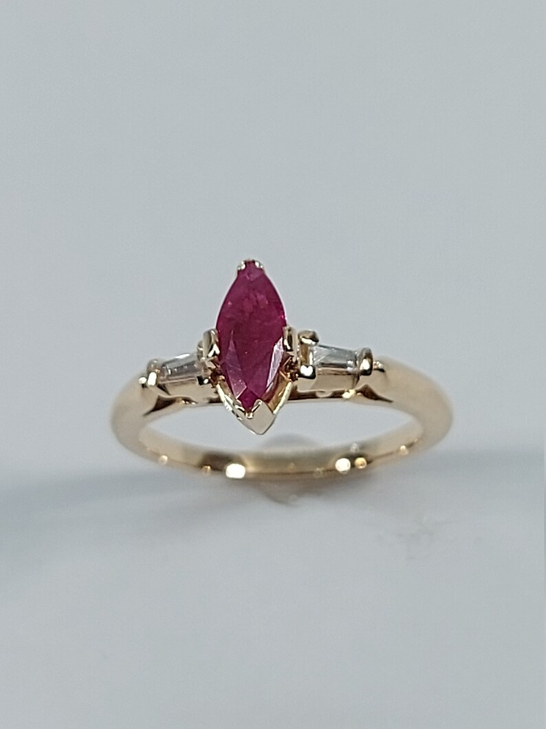May include: A gold ring featuring a marquise-shaped ruby gemstone with two smaller diamond accents.