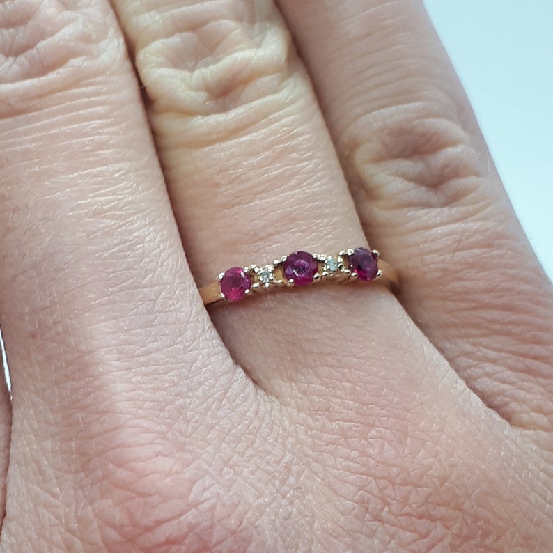 May include: A gold band ring with three red gemstones and two smaller white gemstones.