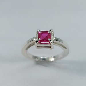 Peut inclure: Une bague en argent avec une pierre précieuse rose vif de forme carrée sertie dans un sertissage en argent.