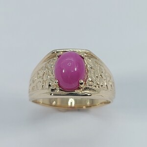 Op de afbeelding: Een gouden ring met een roze ovale edelsteen gezet in een getextureerde band.