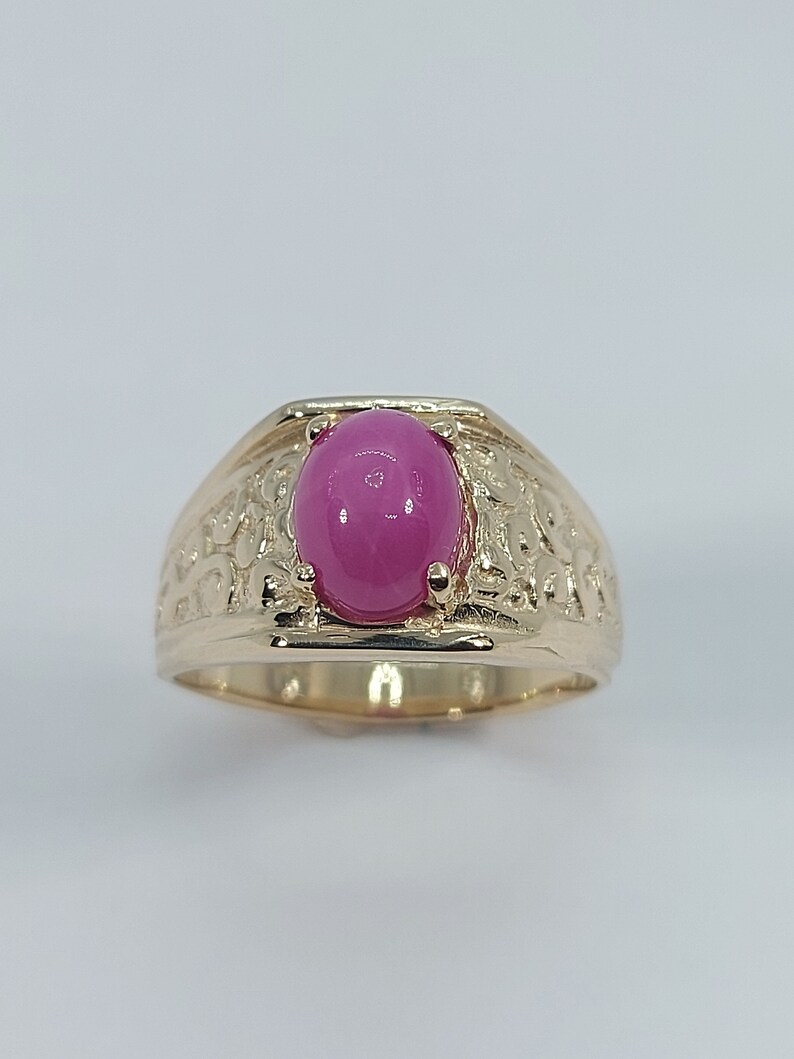 Op de afbeelding: Een gouden ring met een roze ovale edelsteen gezet in een getextureerde band.