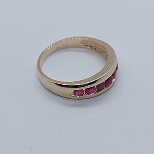 May include: A gold band ring with a row of red ruby stones set in the band.