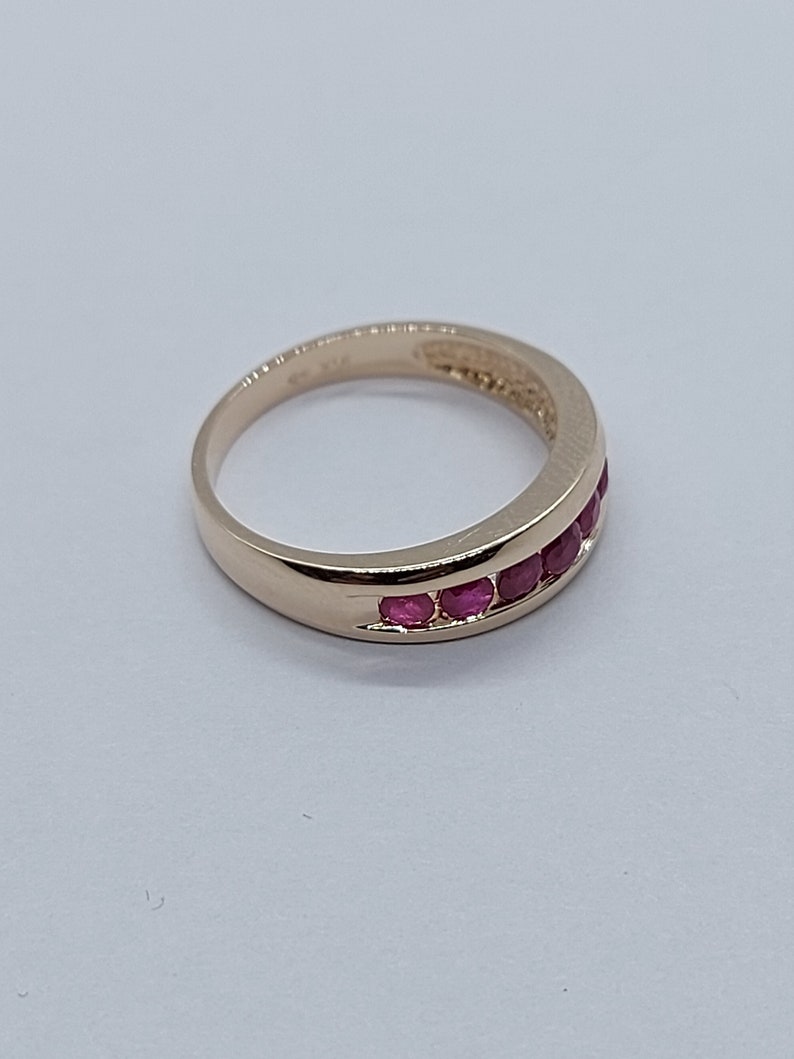 May include: A gold band ring with a row of red ruby stones set in the band.