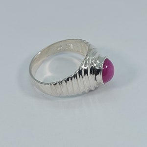 K&ouml;nnte beinhalten: Ein silberner Ring mit einem rosafarbenen Edelstein, der in einem strukturierten Band gefasst ist.