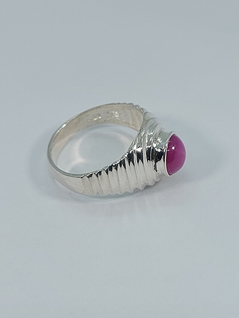 K&ouml;nnte beinhalten: Ein silberner Ring mit einem rosafarbenen Edelstein, der in einem strukturierten Band gefasst ist.